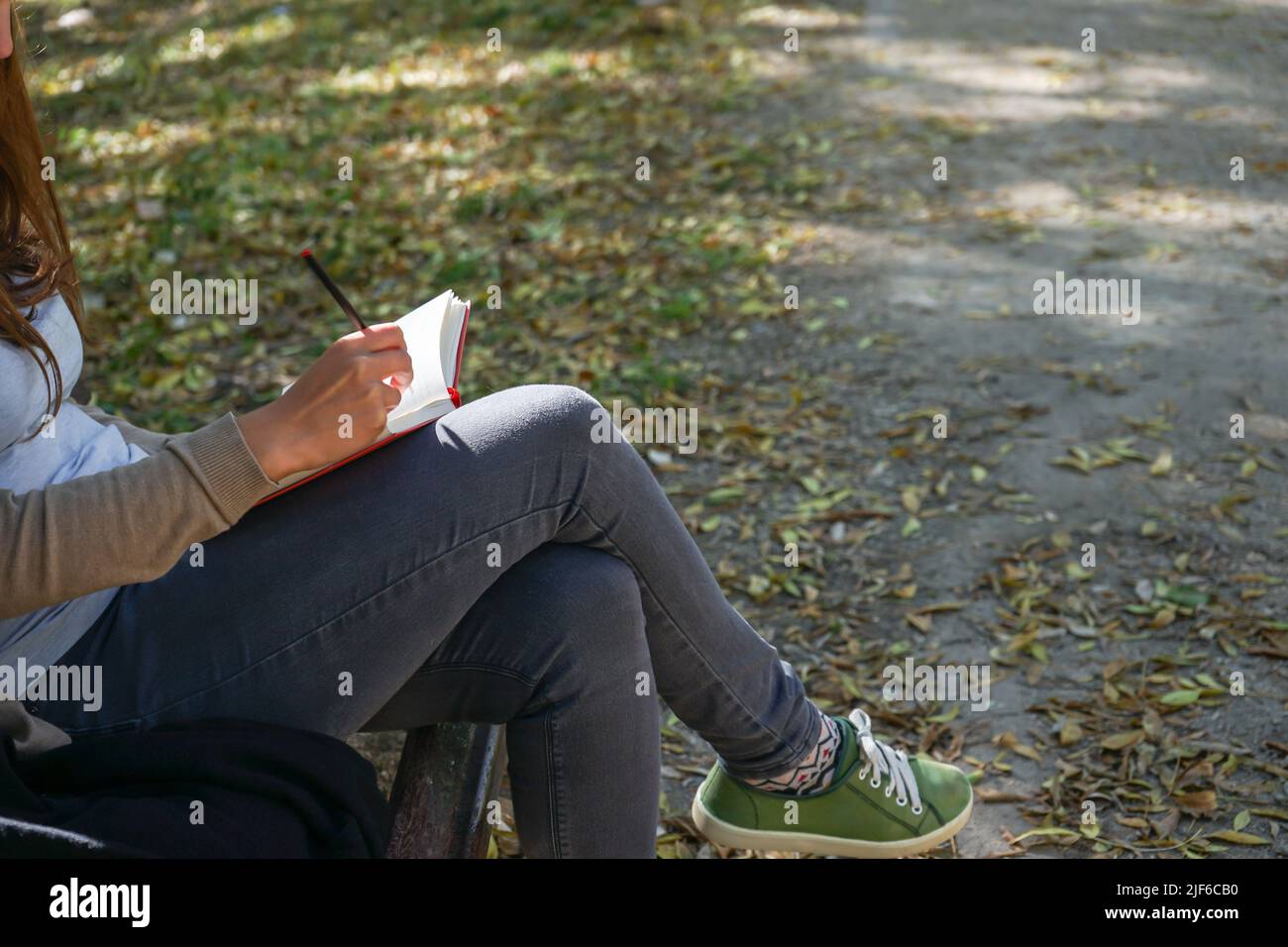 Geballte Frau, die auf einem Notizbuch auf einer Bank in einem Park sitzt Stockfoto