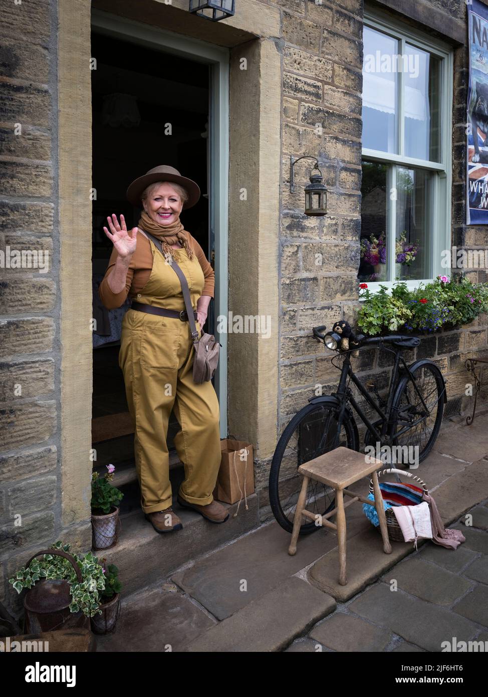 Haworth 1940 nostalgisches Retro-Ereignis mit Lebensgeschichte (Frau im Vintage WW2-Kostüm, die vor der Haustür posiert) - Main Street, West Yorkshire England. Stockfoto