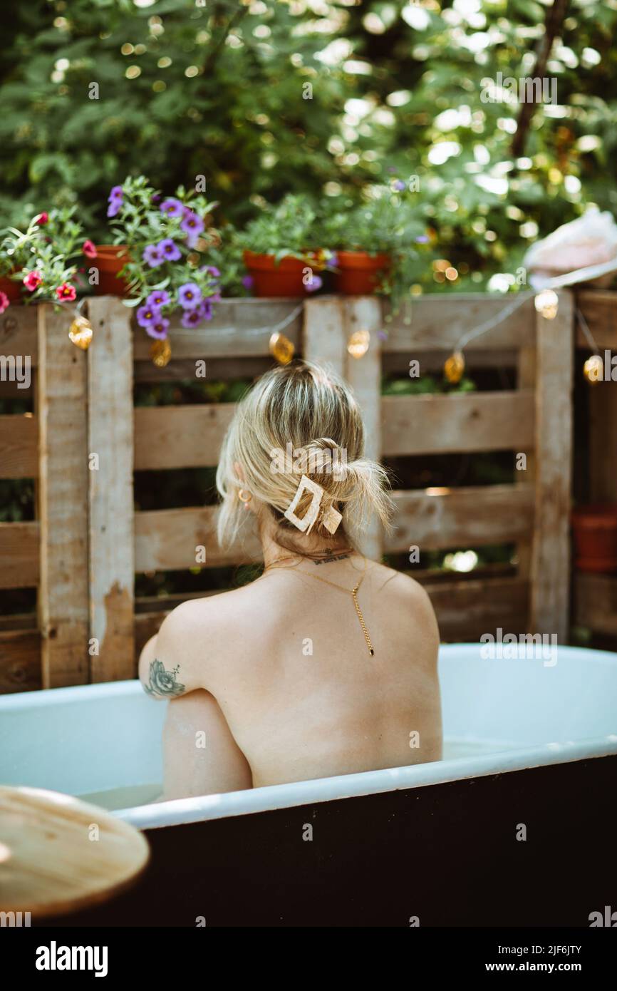 Seitenansicht einer anmutigen Frau im Sommerkleid, die am Tisch auf dem Balkon sitzt und wegschaut Stockfoto
