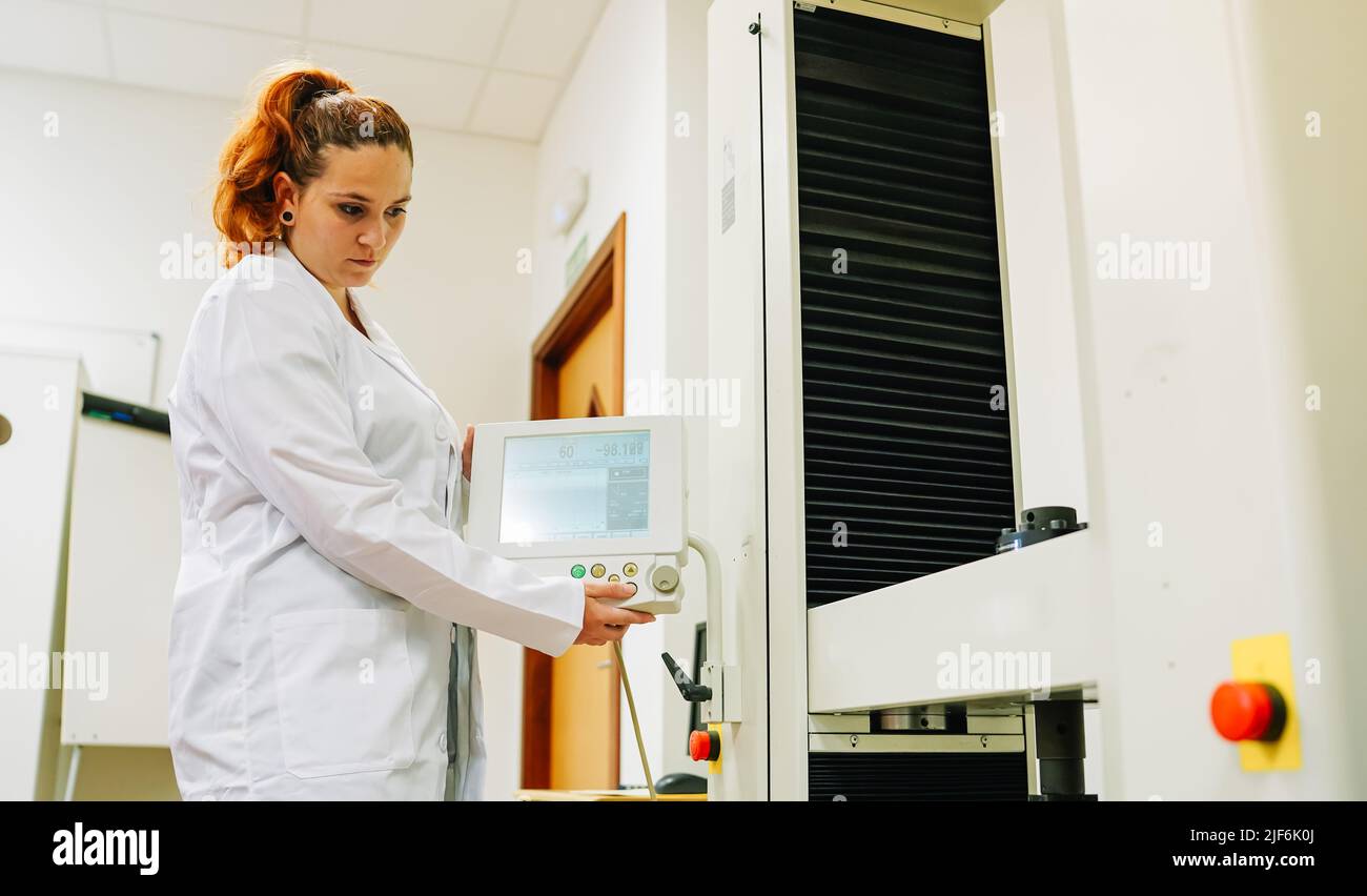 Fokussierte Wissenschaftlerin in medizinischer weißer Uniform, die moderne professionelle Geräte mit Display eindreht, während sie im modernen Lichtlabor arbeitet Stockfoto