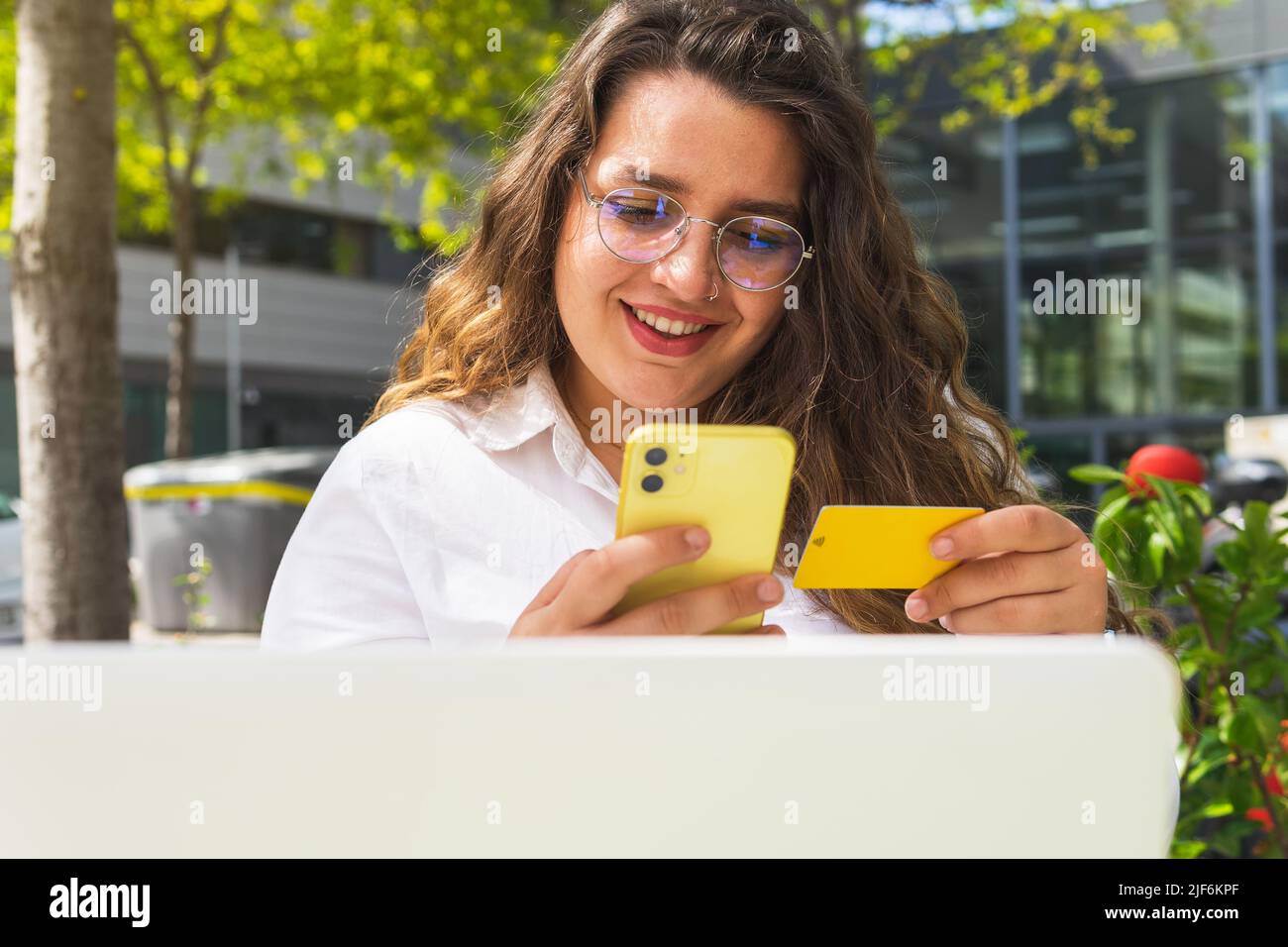 Positive Frau, die mit Kreditkarte online auf dem Laptop bezahlt, während sie am Tisch auf der Terrasse der Cafeteria im Freien sitzt Stockfoto