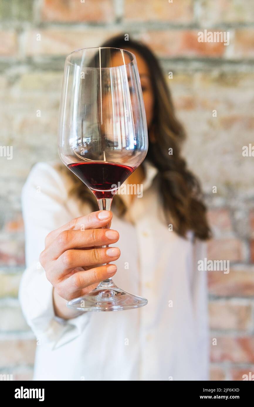 Weicher Fokus einer nicht erkennbaren Sommelierin in weißem Hemd, der im Restaurant einen Glaskelch aus Rotwein an der Backsteinmauer zeigt Stockfoto