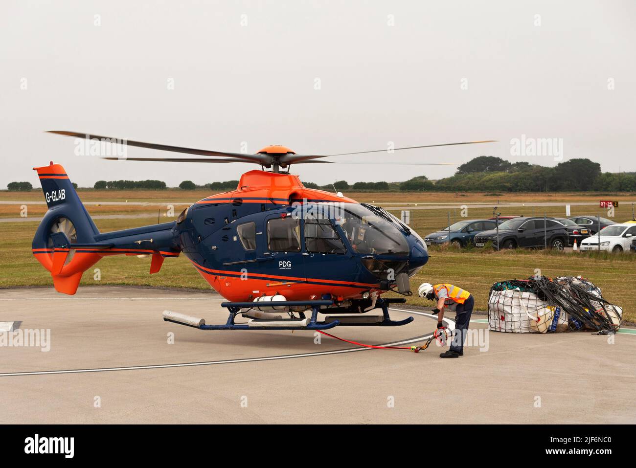 Cornwall, England, UK.2022. Luftlift-Helikopter hebt mit Fracht in einer Schlinge und einem Handsignal vom Personal der Bodencrew ab. Stockfoto
