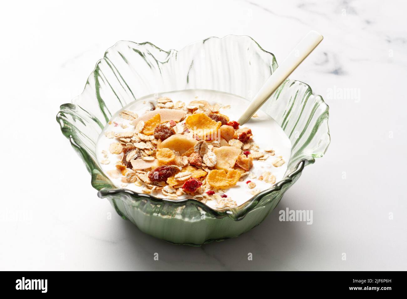 Schüssel mit Joghurt und Frühstückszerealien mit einem Metalllöffel auf einem Tisch Stockfoto