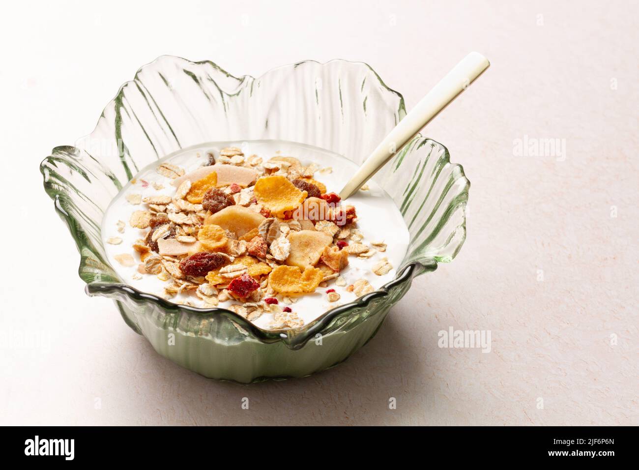 Schüssel mit Joghurt und Frühstückszerealien mit einem Metalllöffel auf einem Tisch Stockfoto