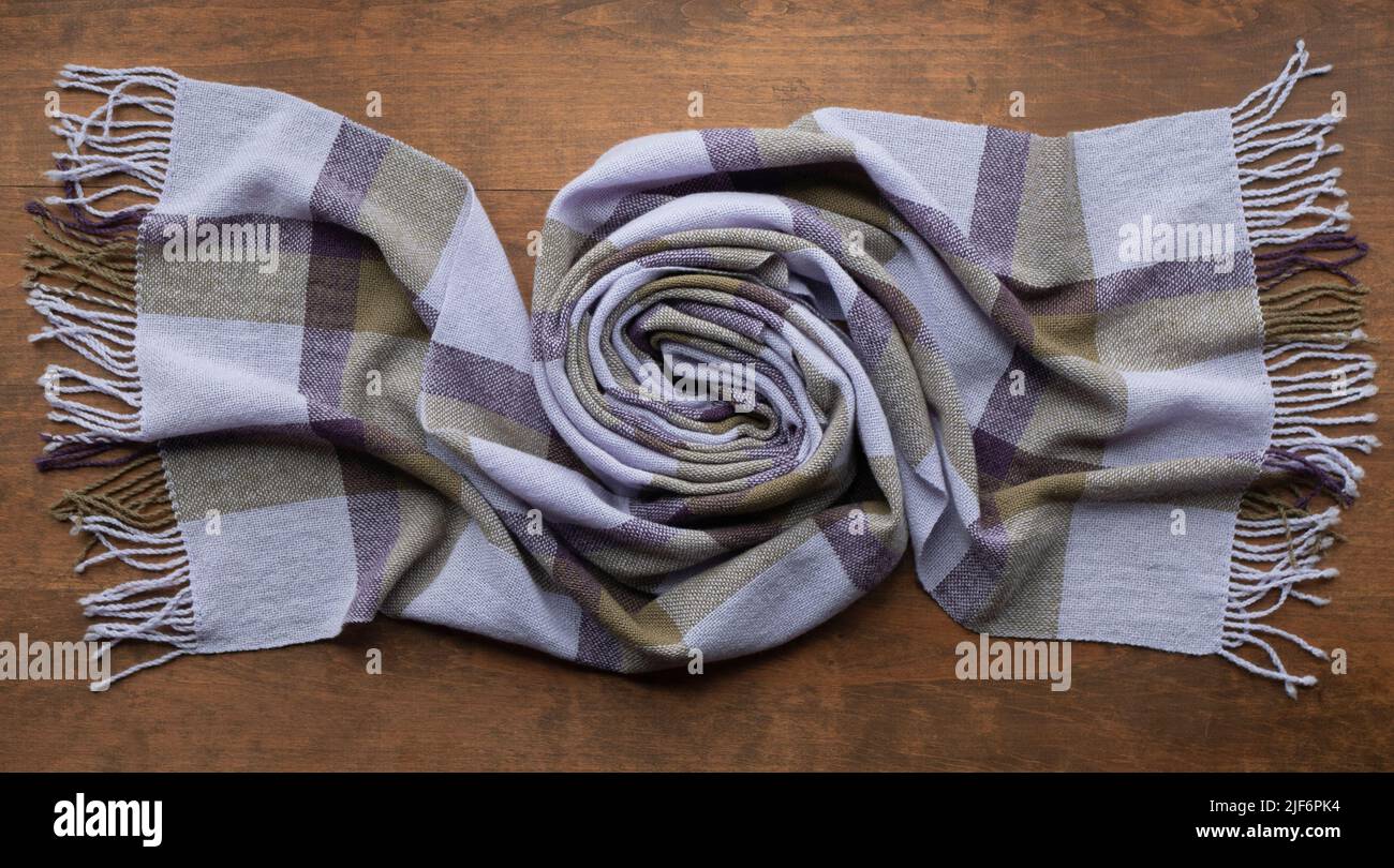 Gefalteter Schal oder Schal in lila, lila und olivfarbener Farbe mit Fransen auf Holztisch. Modisches Accessoire Stockfoto