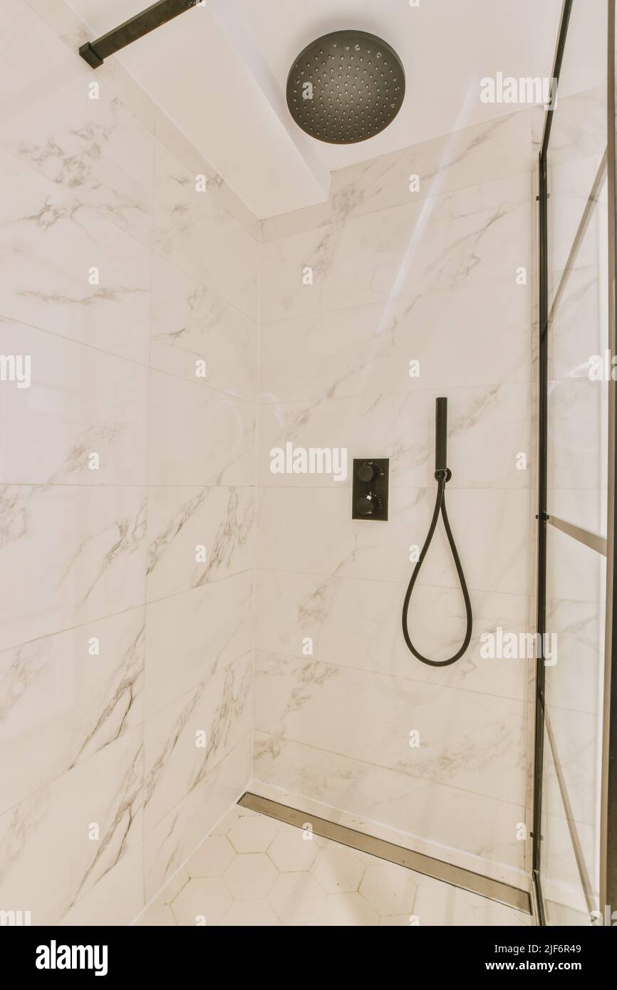 Duschhähne, die an der gefliesten Wand in der Nähe der Glaswand und der Zierschwanzwand im Waschraum zu Hause angebracht sind Stockfoto