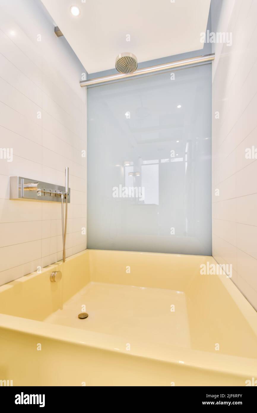Große quadratische gelbe Badewanne mit Chrom-Duschkopf im modernen Badezimmer mit weiß und blau gefliesten Wänden Stockfoto