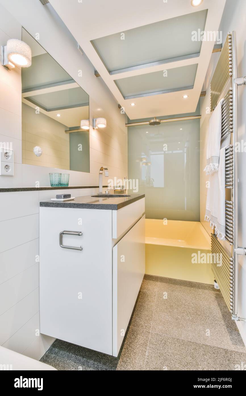 Badewanne in leuchtendem Gelb und Waschbecken mit Chromarmaturen im modernen beleuchteten Badezimmer mit weiß gefliesten Wänden und Spiegel Stockfoto