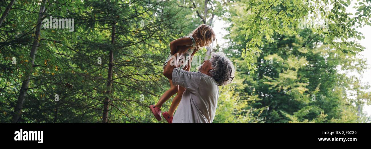 Breitbild-Bild der schönen Verbindung zwischen einem Großvater und einer Enkelin - Opa hob ihr Enkel hoch oben in der Luft draußen in grüner Summe Stockfoto