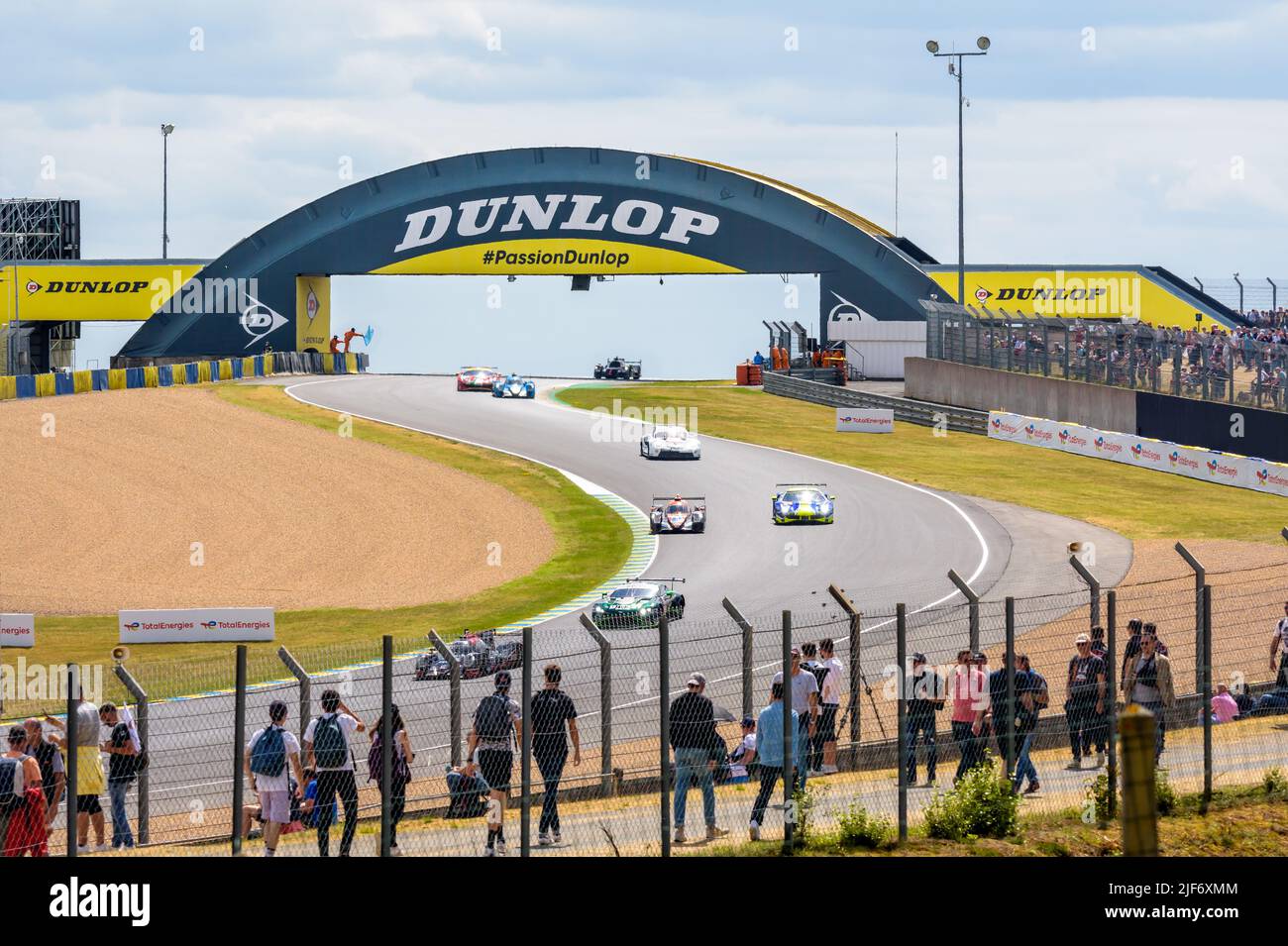 Rennwagen fahren unter der Dunlop-Fußgängerbrücke hindurch und fahren während der 24 Stunden von Le Mans die Kurven auf der Rennstrecke Circuit de la Sarthe hinunter. Stockfoto