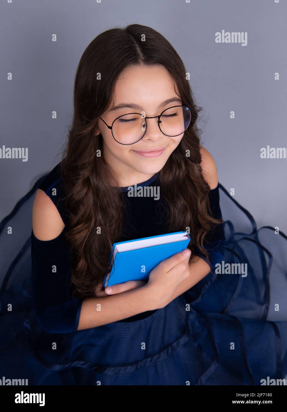Träumende Schülerin in Kleid halten Buch und Copybook bereit zu lernen. Schulkinder träumen auf isoliertem grauen Hintergrund. Stockfoto