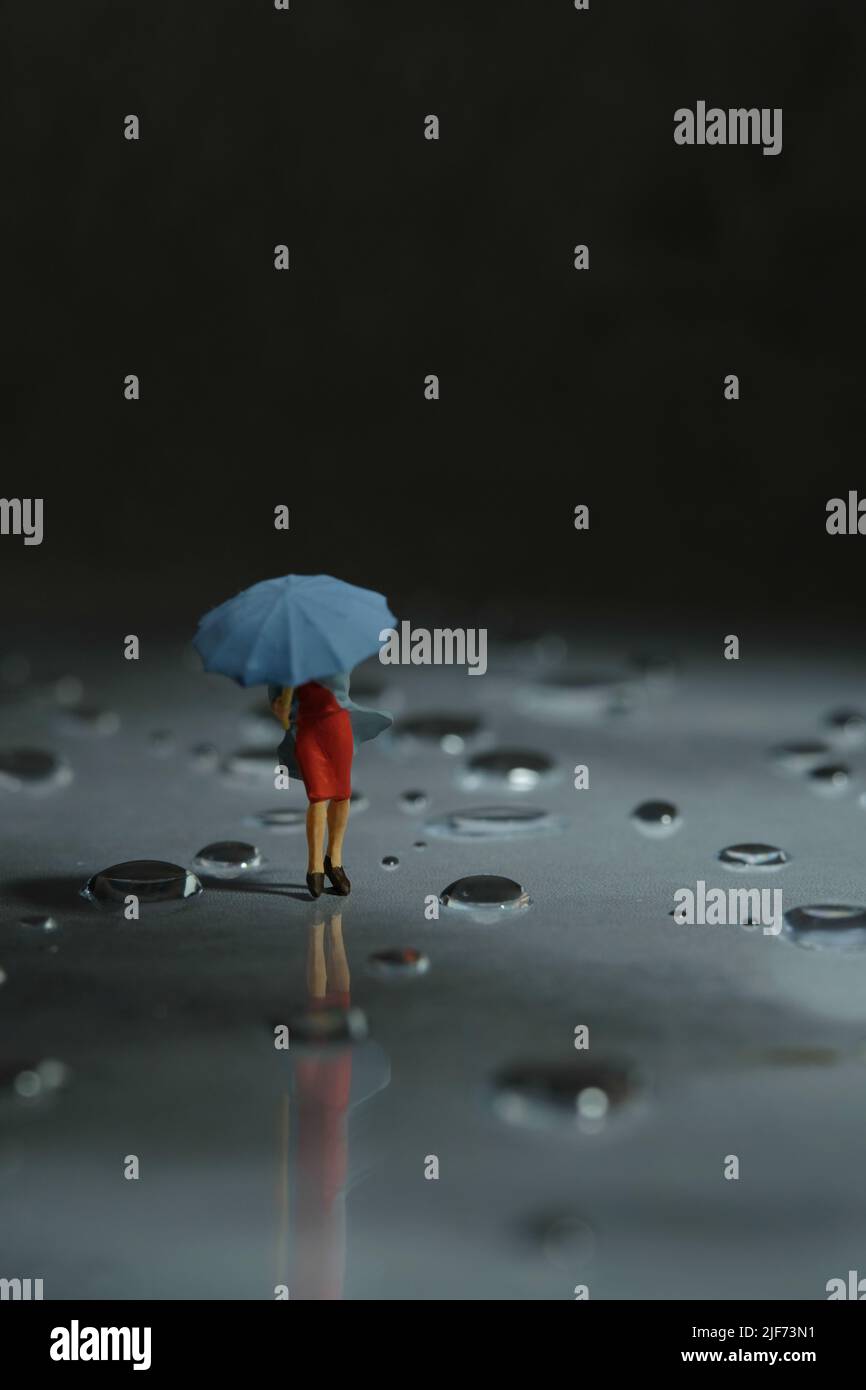 Miniatur Menschen Spielzeug Figur Fotografie. Eine Frau, die einen Regenmantel mit Regenschirm trägt und während eines Sturms auf der Straße läuft, gegen einen sehr starken Wind. Stockfoto