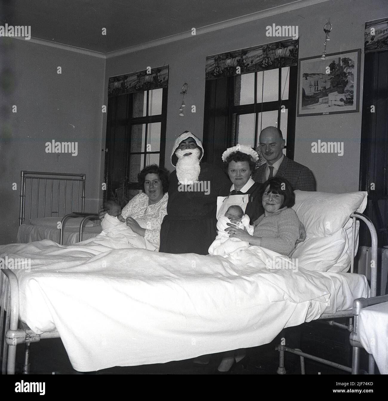 1965, historisch, ein Weihnachtsvater, der eine Entbindungsstation besucht und für ein Foto steht, beisde eine Krankenschwester und zwei neue Mütter, die mit ihren neuen Babys in Krankenhausbetten liegen, Fife, Schottland, Großbritannien. Stockfoto