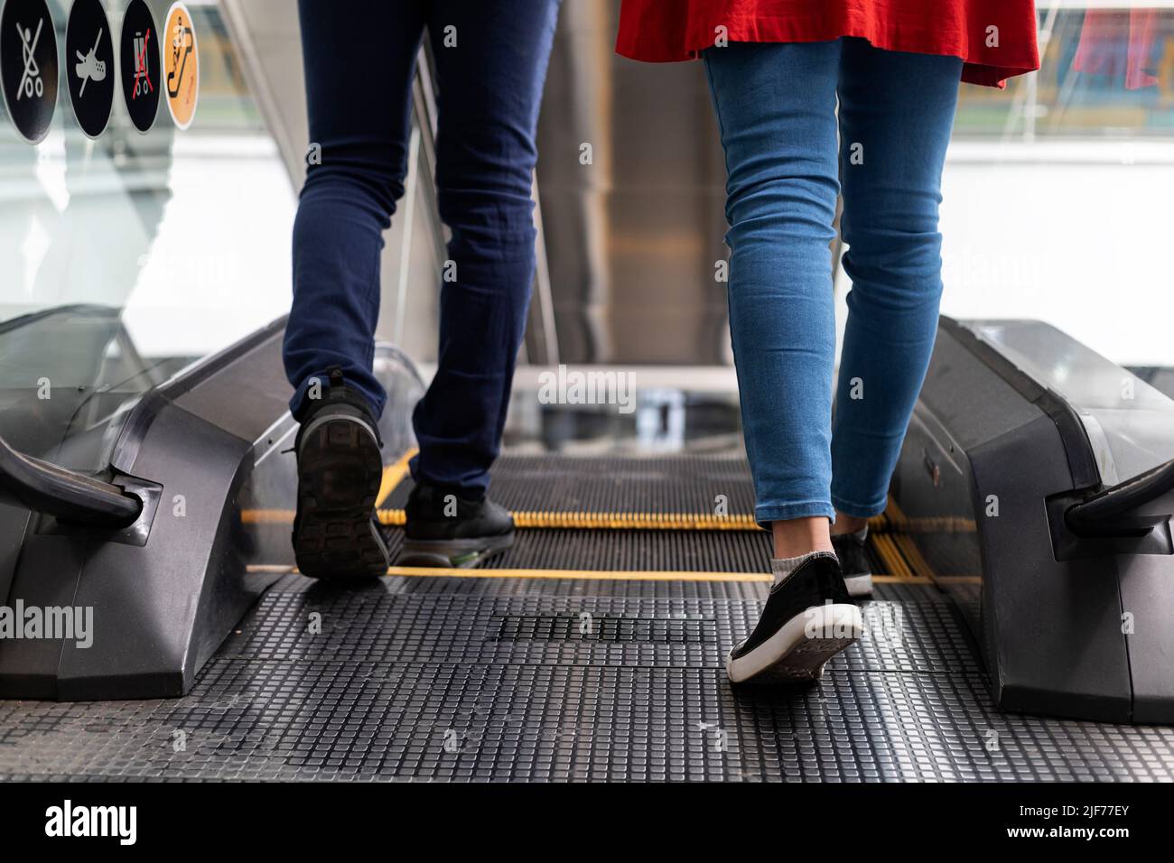 Nicht erkennbares junges lateinamerikanisches Paar, das zusammen zurück nach hinten geht, um mit der Rolltreppe zu fahren. Mittlere kurze Aufnahme ihrer Beine Stockfoto