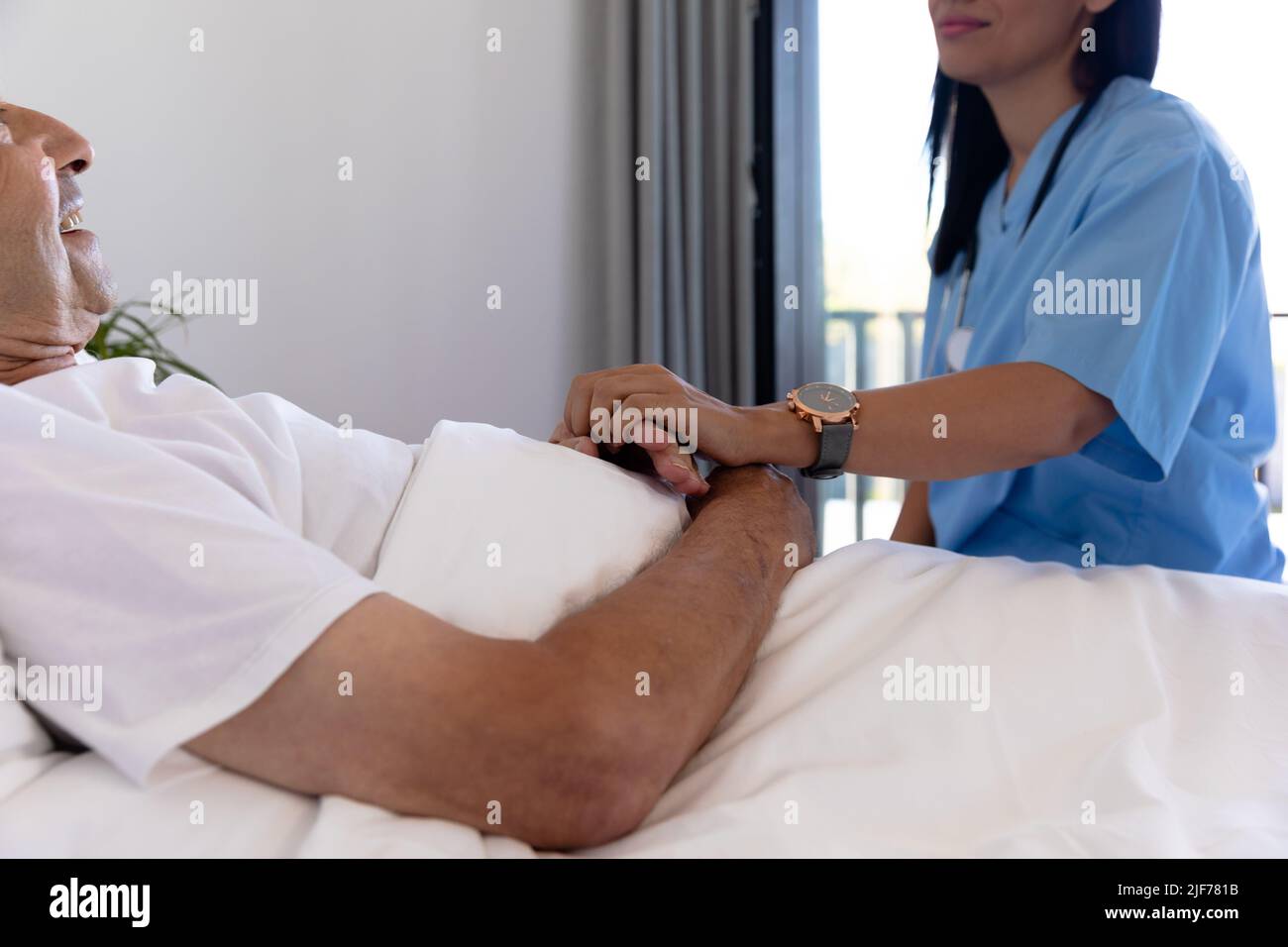 Mittlerer Abschnitt einer birazialen Gesundheitshelferin, die einen älteren kaukasischen Mann auf dem Bett unterstützt Stockfoto