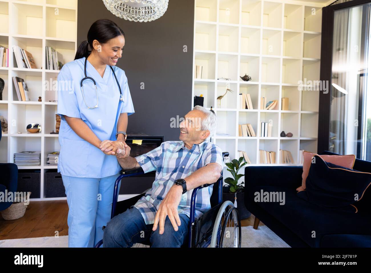 Biraziale Gesundheitshelferin, die einen kaukasischen älteren Mann unterstützt, der auf dem Rollstuhl sitzt Stockfoto