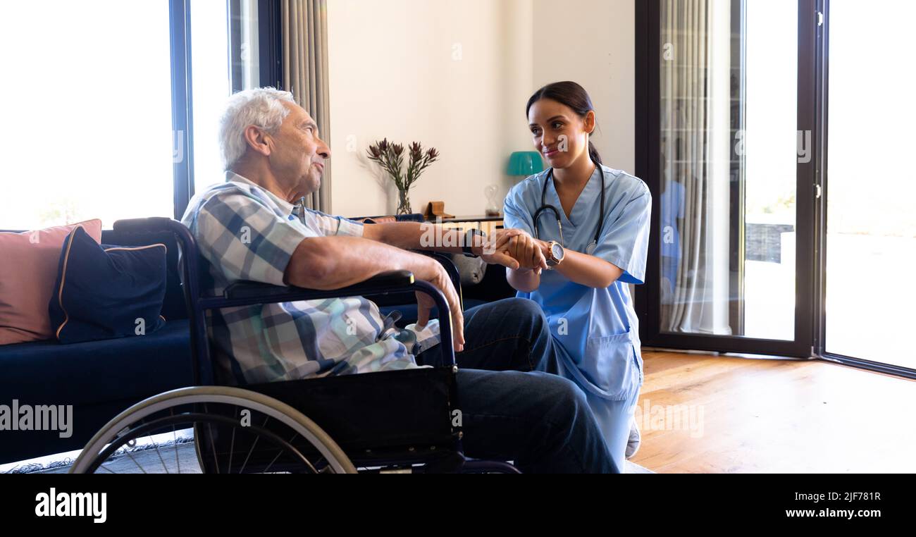 Biraziale Gesundheitshelferin, die einen kaukasischen älteren Mann unterstützt, der auf dem Rollstuhl sitzt Stockfoto