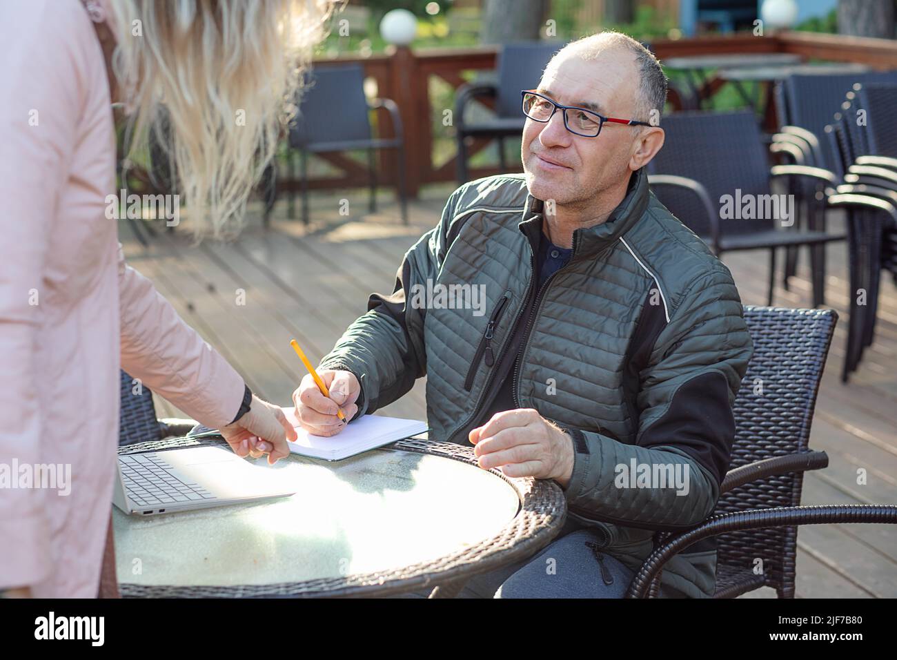Porträt eines Mannes mittleren Alters, der im Café am Tisch sitzt, den Stift bereit hält, eine Notiz in den Notizblock zu schreiben, und die Frau anschaut. Stockfoto