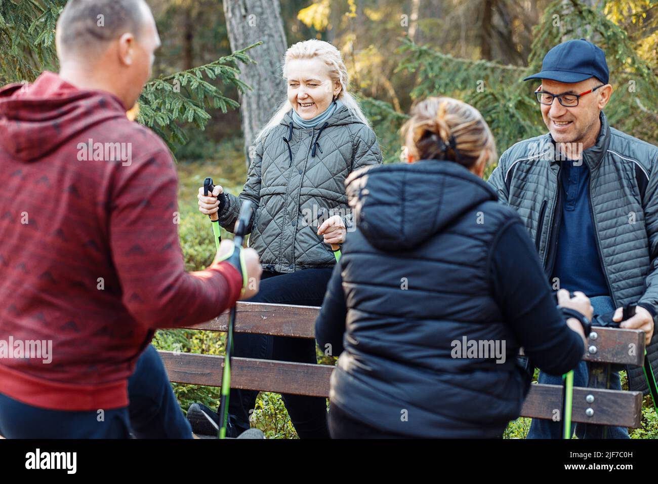 Ältere und ältere Menschen lernen skandinavisches Gehen mit professionellen Stöcken im Wald in der Nähe von Zaun. Schulungen Stockfoto
