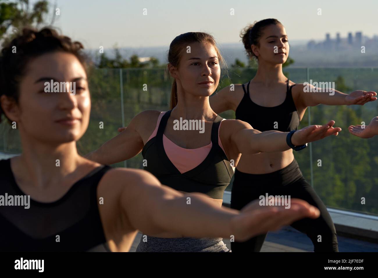 Fit gesunde sportliche Frauen stehen in Yoga-Kriegerpose in der Gruppenklasse im Freien. Stockfoto