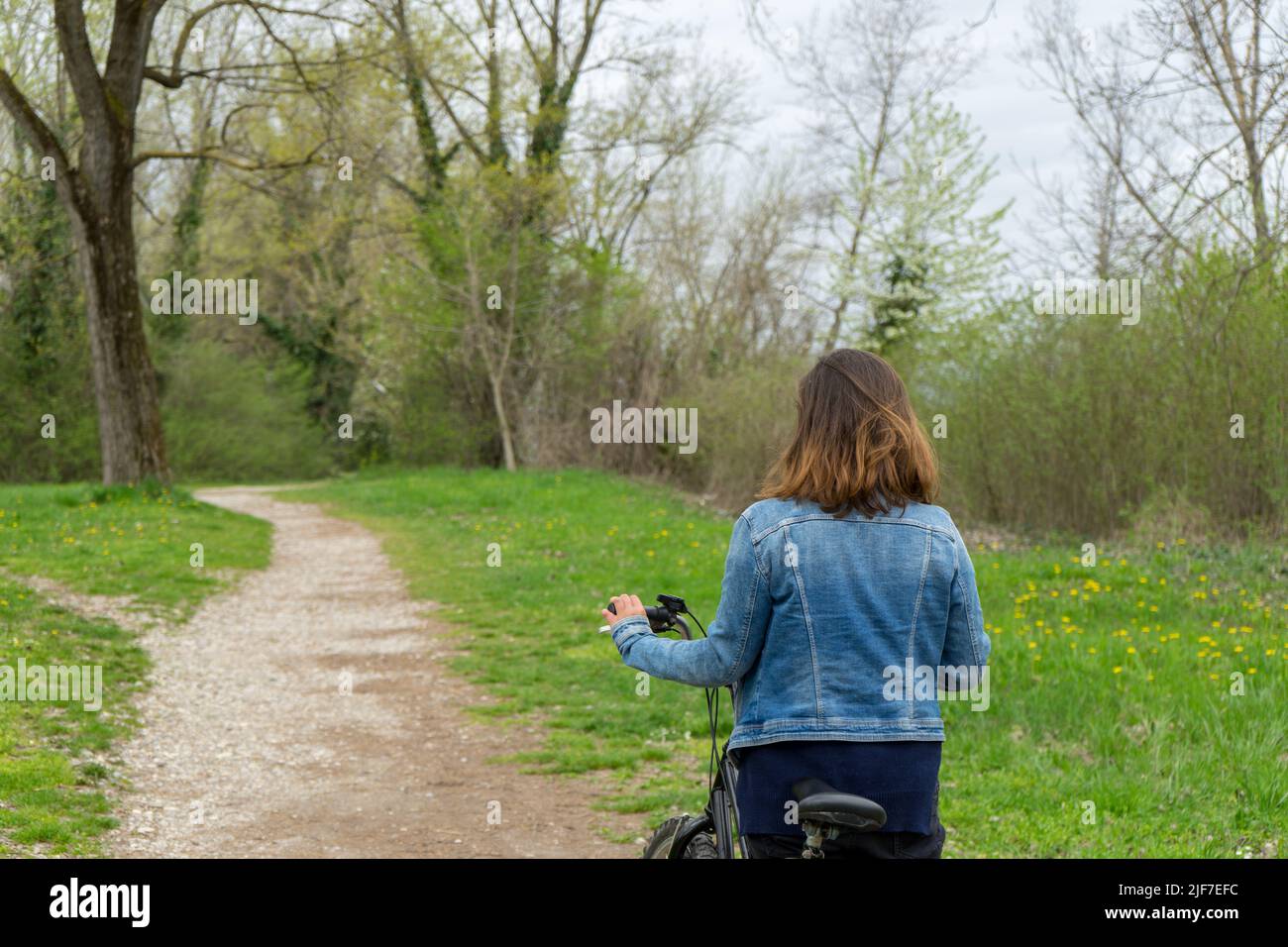 Frau, die auf einer unbefestigten Straße im Wald auf der Seite ihres Fahrrads steht. Stockfoto