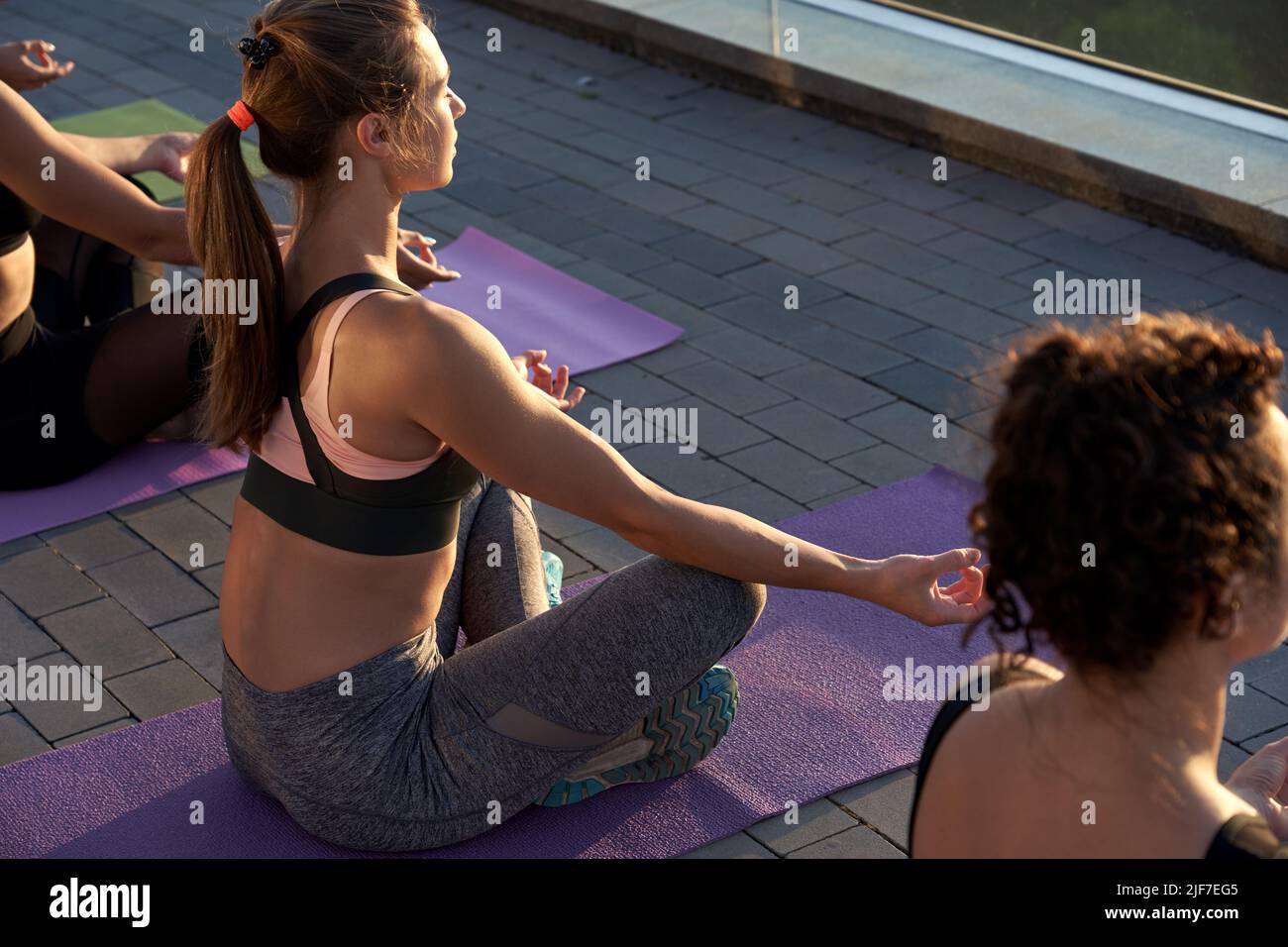Multiethnische junge Frauen meditieren bei einem Yoga-Kurs bei Sonnenaufgang im Freien. Stockfoto