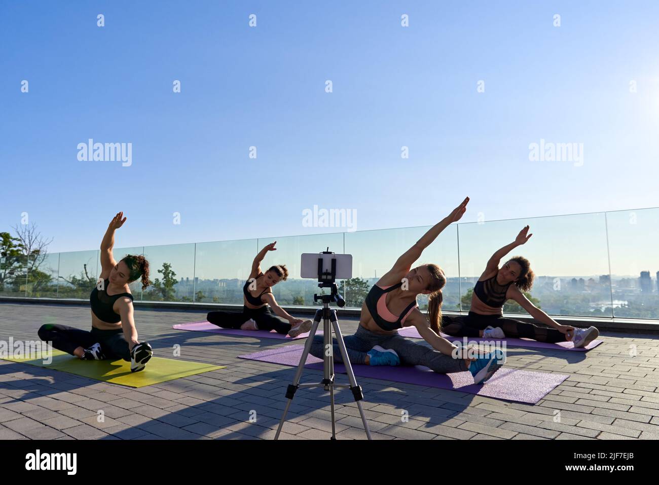 Diverse Frauen Gruppe schießen online Stretching Klasse Tutorial im Freien am Telefon. Stockfoto