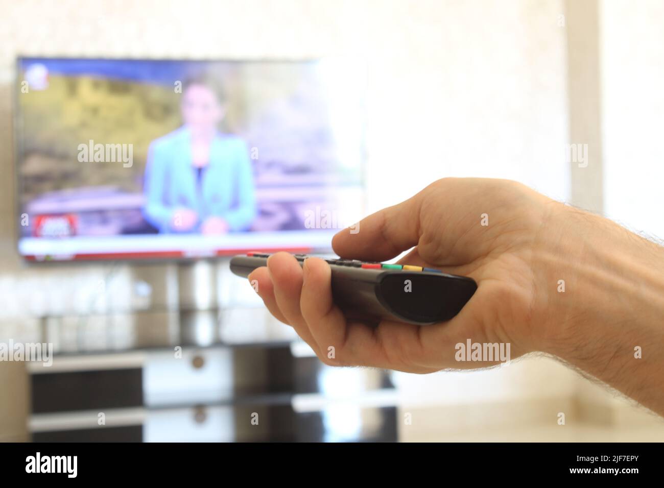 Fernbedienung, ein Mann mit einer Fernbedienung in der Hand schaltet die Sender auf dem fernseher. Stockfoto