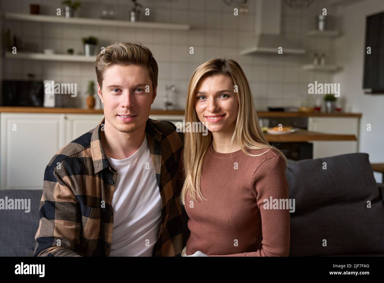 Glückliches junges Millennial Paar Bonding beim Blick auf die Kamera, die zu Hause auf dem Sofa sitzt. Stockfoto