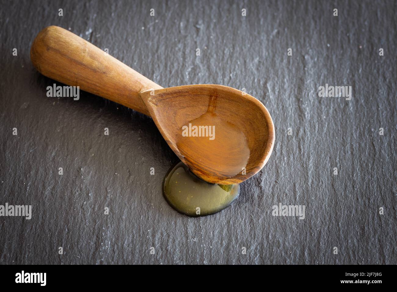 Honig fließt aus einem Holzlöffel auf eine schwarze Unterlage Stockfoto