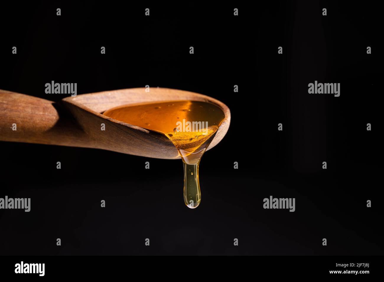 Honig tropft aus einem Holzlöffel vor einem schwarzen Hintergrund Stockfoto