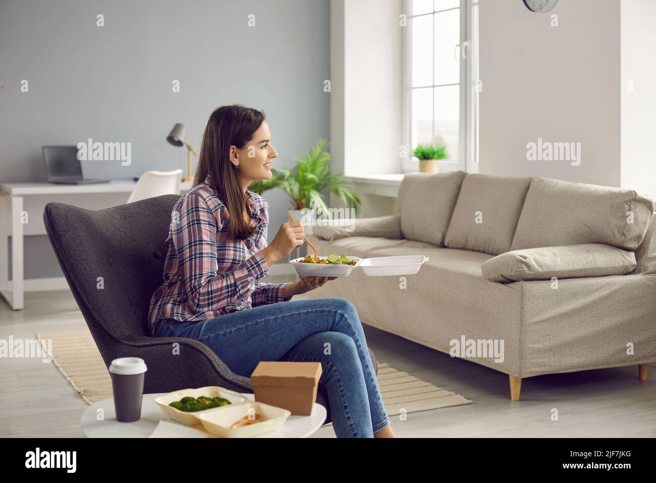 Die junge Frau zu Hause genießt während des Mittagessens eine köstliche Mahlzeit vom Lieferservice. Stockfoto