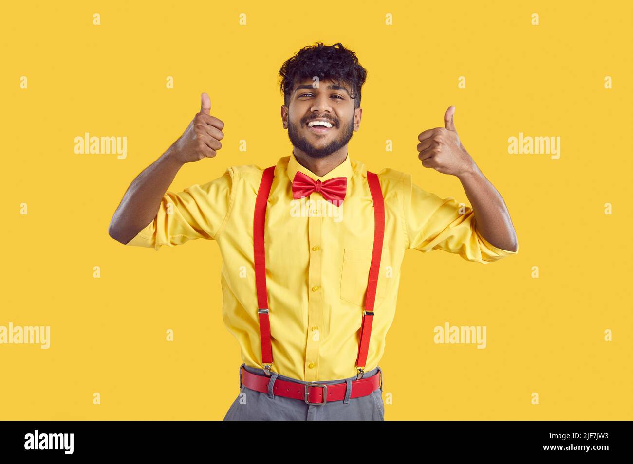 Glücklicher, gutaussehender junger Inder in Hemd und Fliege, der Daumen hoch und lächelnd zeigt Stockfoto