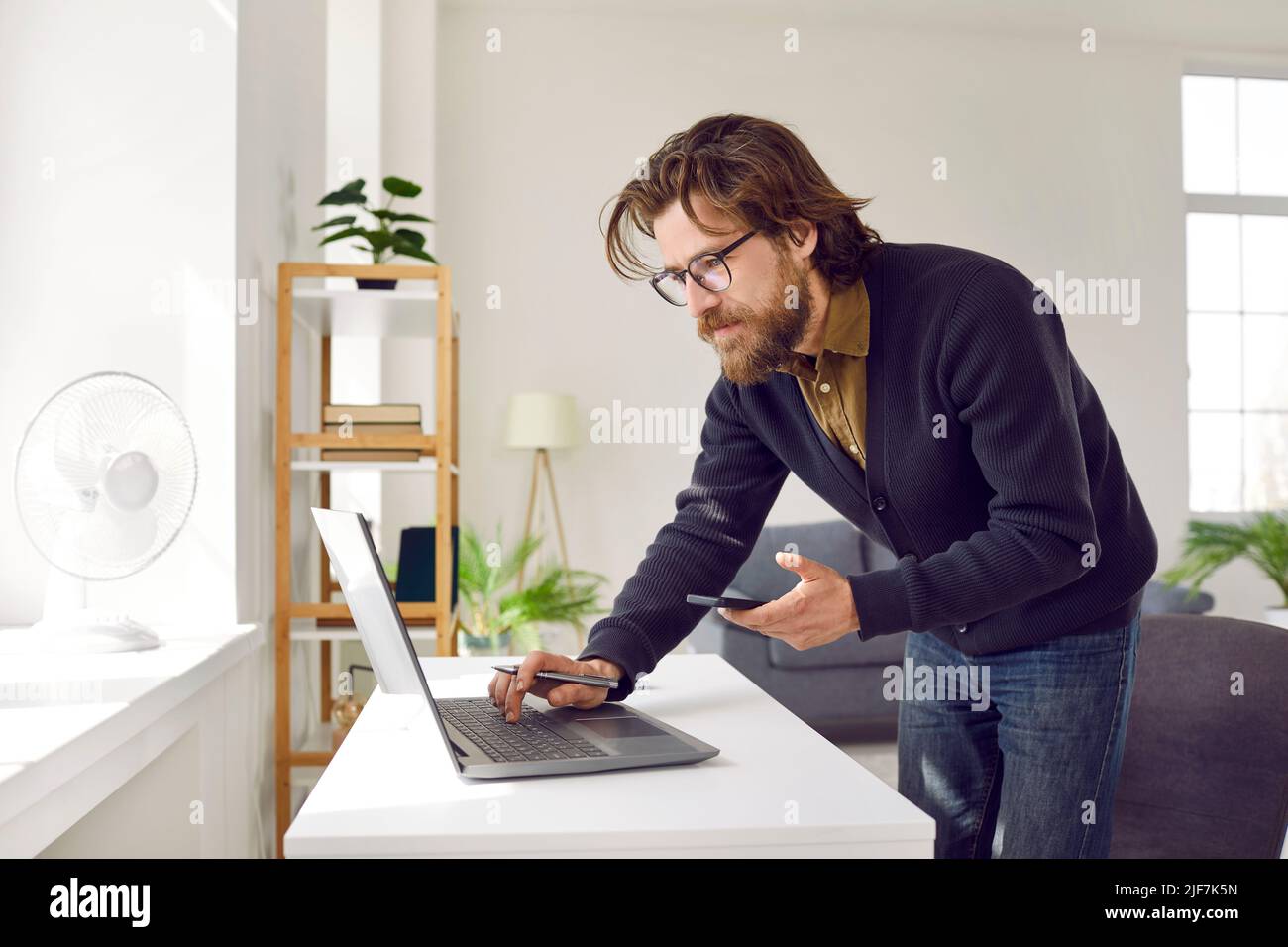 Fokussierter, intelligenter Geschäftsmann mit Laptop und Mobiltelefon, der von zu Hause aus arbeitet. Stockfoto