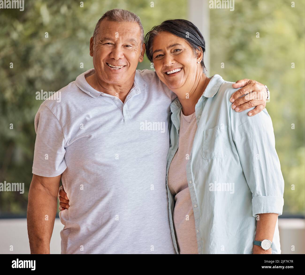 Porträt eines glücklichen älteren Paares, das lächelt und zu Hause vor einem Fenster steht und die Kamera anschaut. Reife hispanische Mann und Frau teilen romantisch Stockfoto