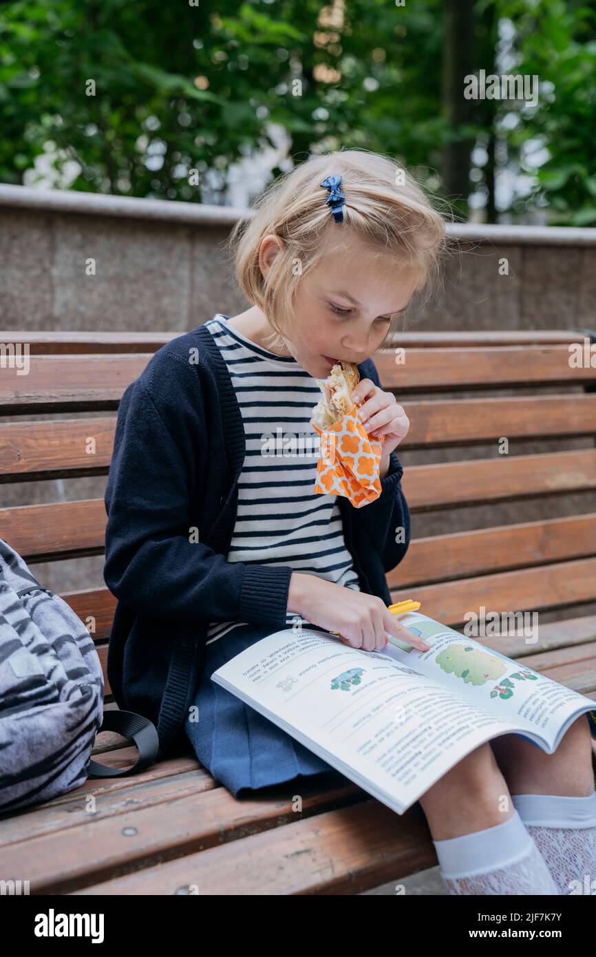 Eine Schülerin isst im Park ein Sandwich und macht ihre Hausaufgaben. Stockfoto