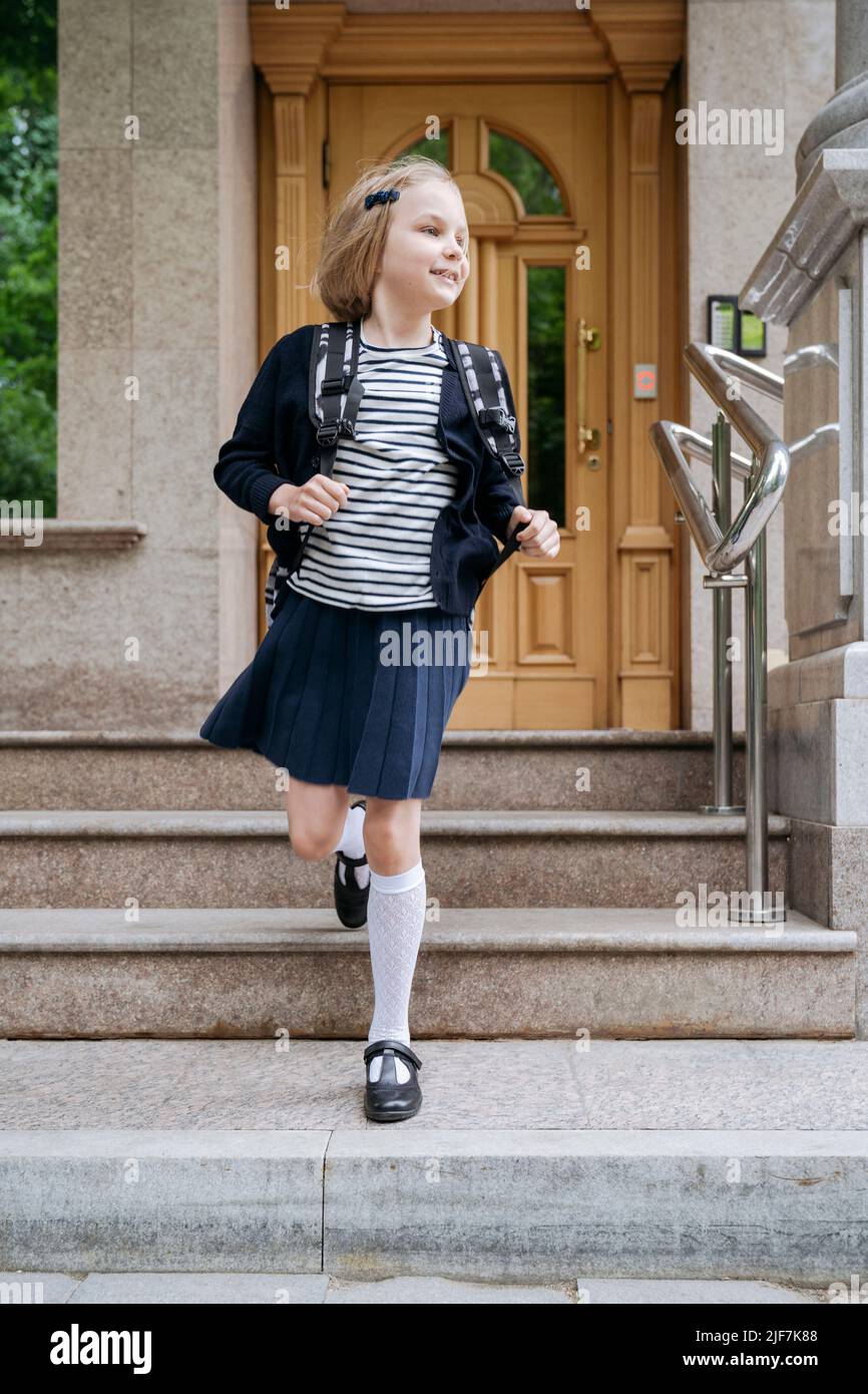 Ein fröhliches Schulmädchen verlässt nach dem Unterricht die Schule. Stockfoto