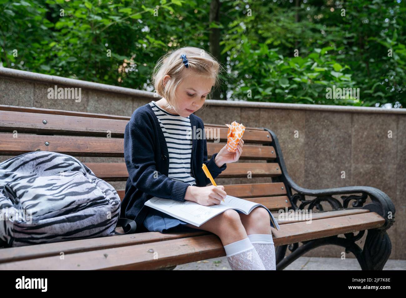 Das Mädchen macht ihre Hausaufgaben und isst ein Sandwich im Park. Stockfoto