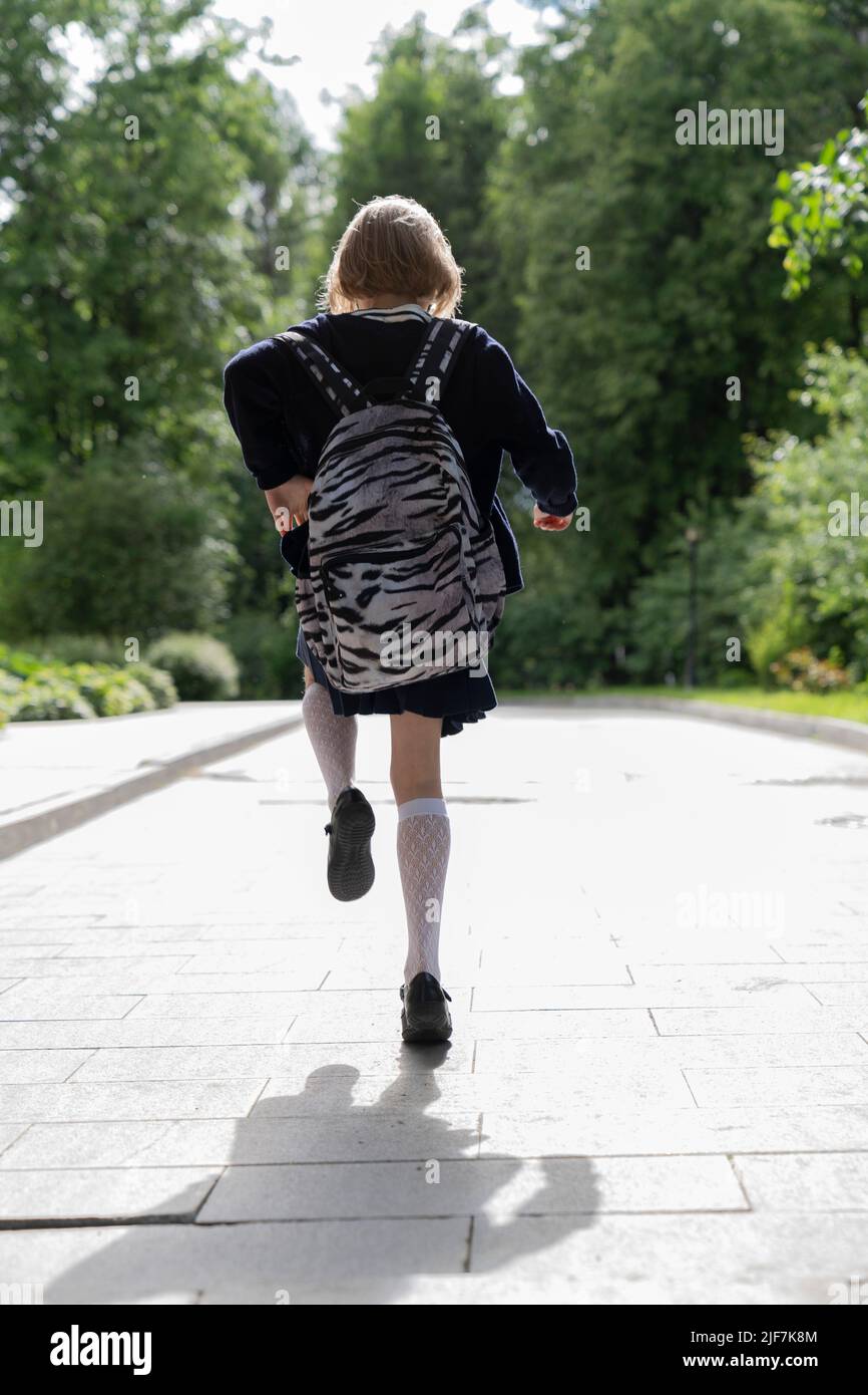 Ein laufendes Mädchen in einer Schuluniform und einer Schultasche von hinten. Stockfoto
