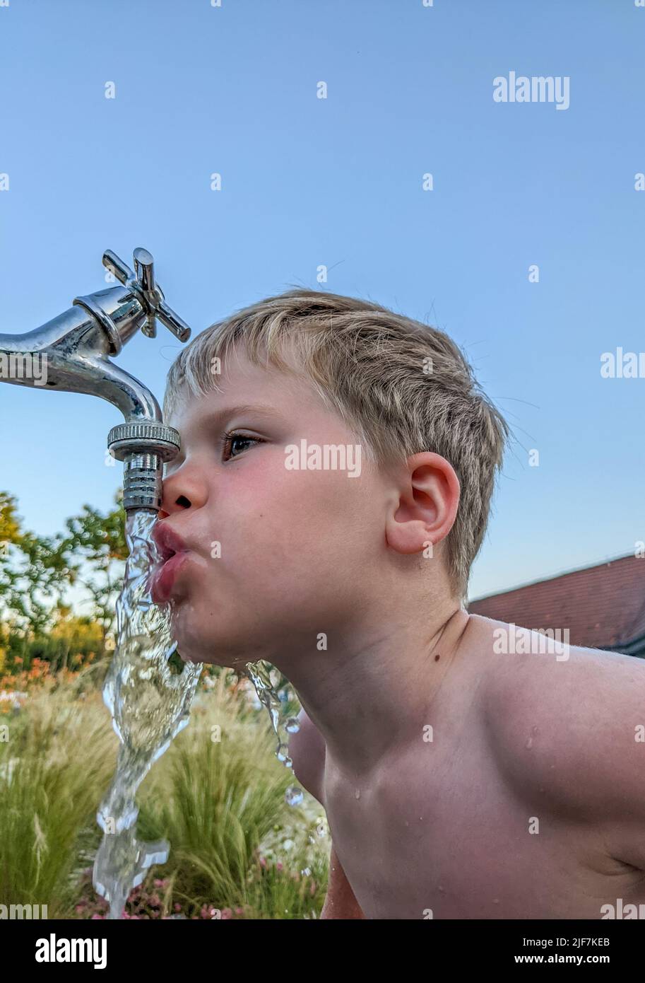 Kleiner Junge trinkt Wasser auf der Straße aus dem Wasserhahn Stockfoto