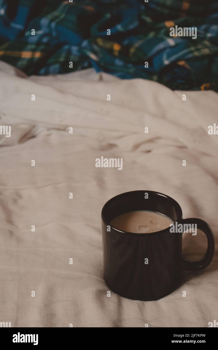 Vertikale dunkle Tasse mit Latte in einem bequemen Bett Stockfoto