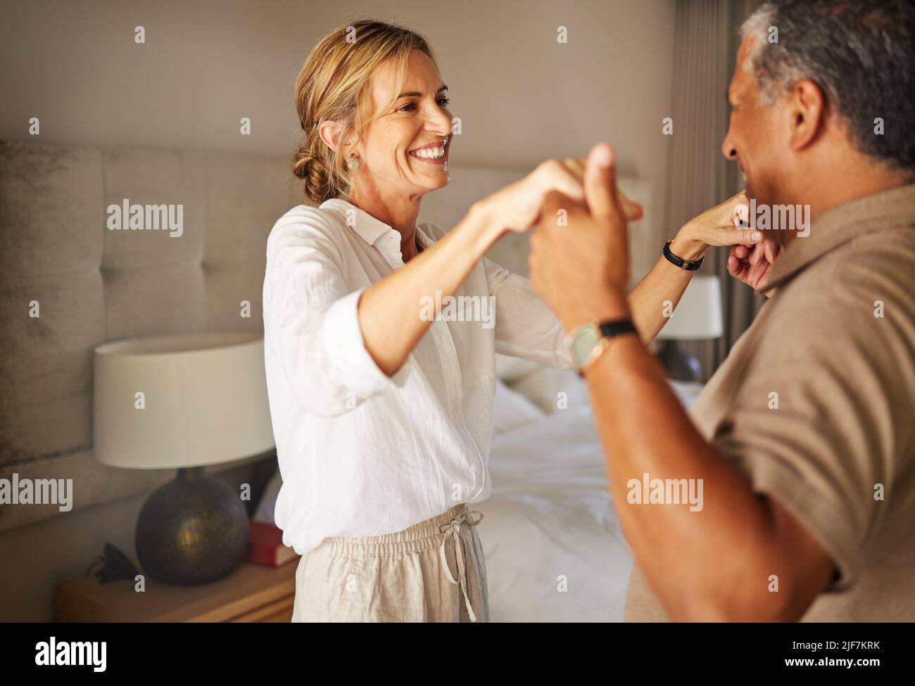Ein älteres interrassisches Paar, das in einem Hotelzimmer zusammen in einem romantischen Urlaub tanzt. Älterer hispanischer Mann und kaukasische Frau, die lächeln und anspielen Stockfoto