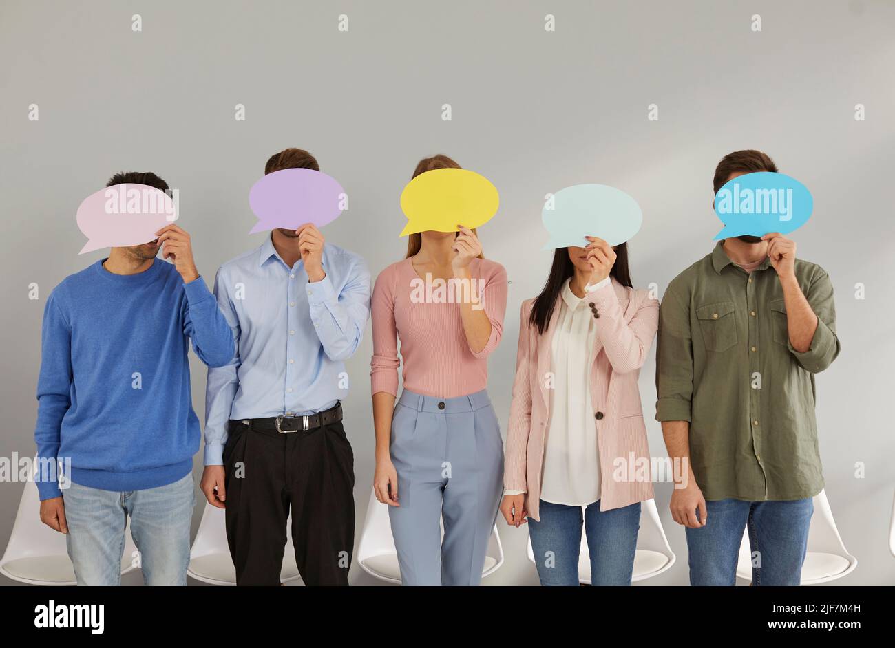 Fünf junge Männer, die in Reihe stehen, verbergen ihre Gesichter hinter leeren farbigen Sprechblasen. Stockfoto