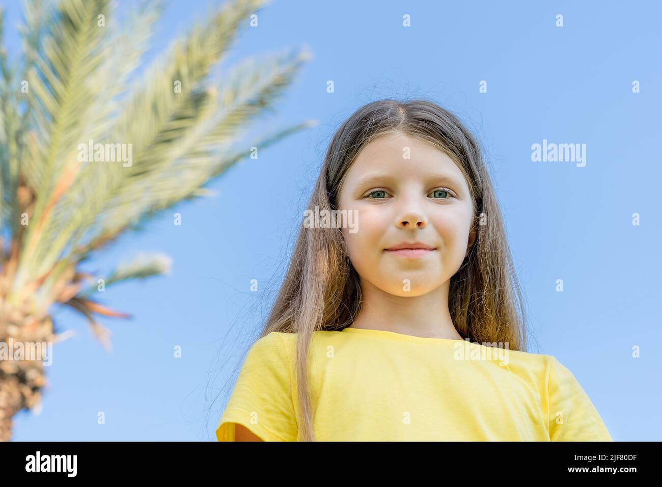 Mädchen in einem gelben T-Shirt auf einem Hintergrund von Palmen im Sommer. Stockfoto