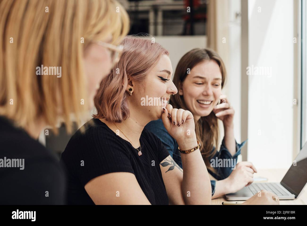 Junge Programmiererin mit Hand am Kinn, die mit Kollegen im Tech-Start-up-Büro zusammenarbeitet Stockfoto