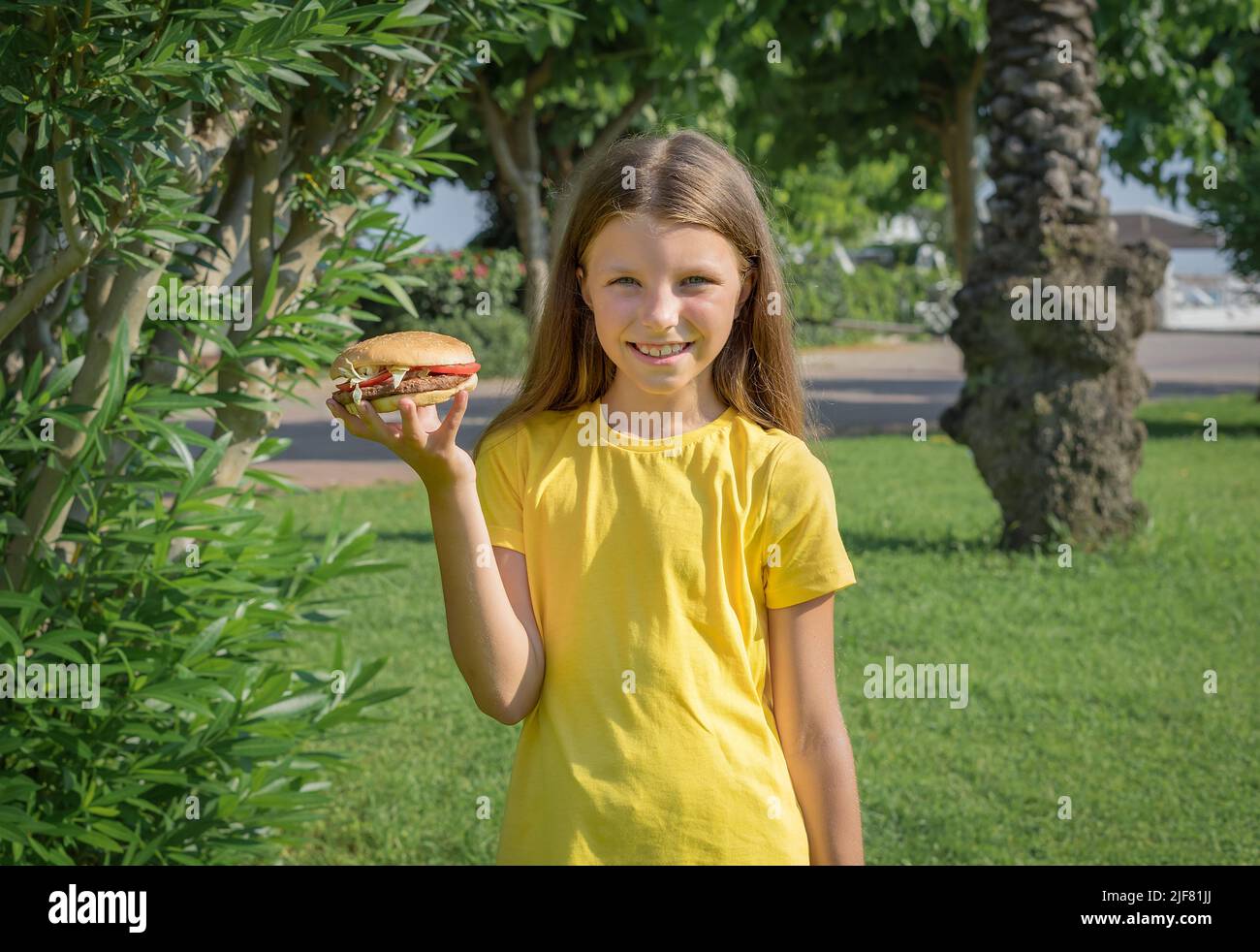 Fröhliches Teenager-Mädchen, das im Park im Freien einen Burger isst. Stockfoto