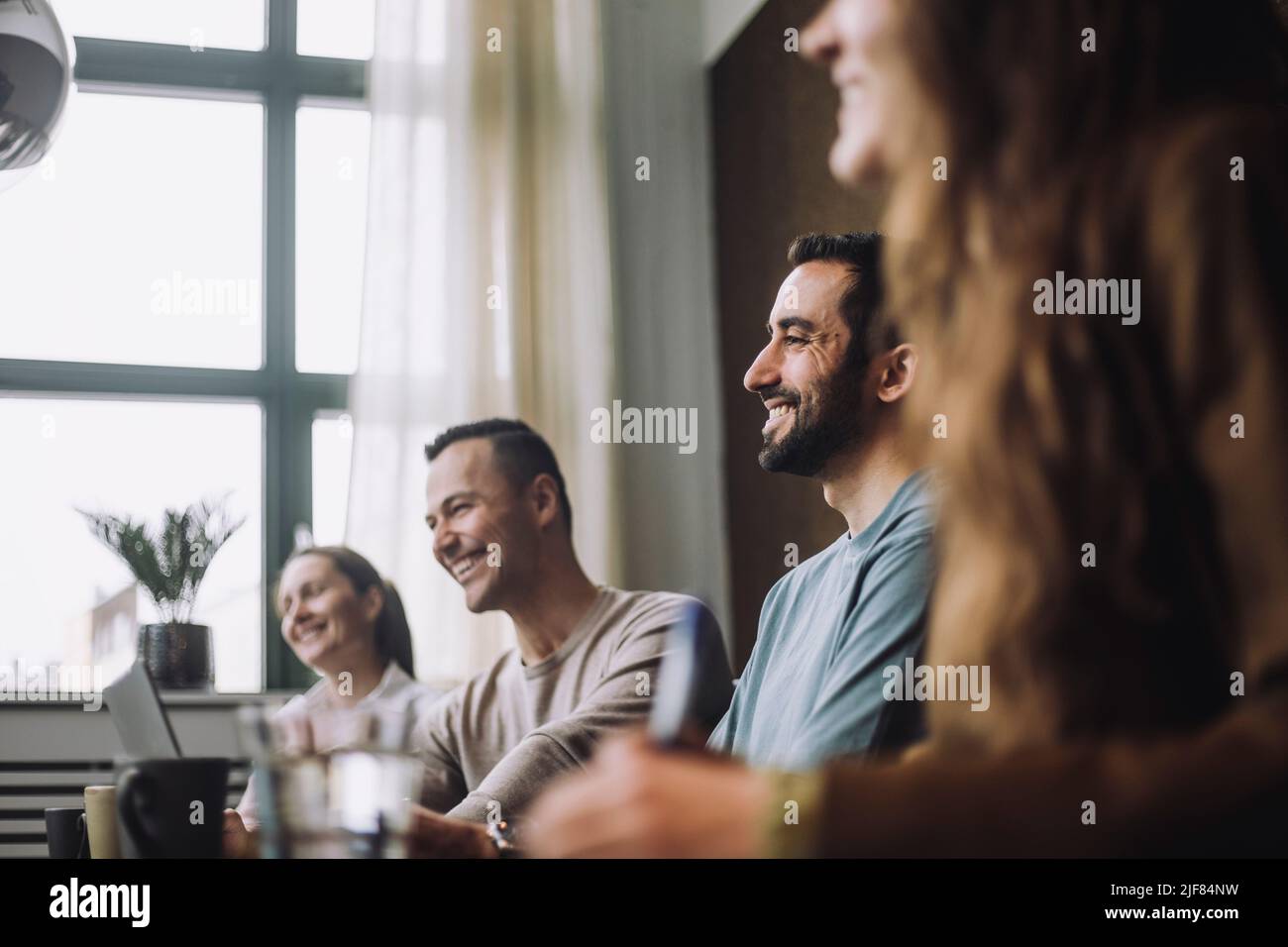 Glücklicher Geschäftsmann mit mittlerem Erwachsenenalter, der im Besprechungsraum von männlichen und weiblichen Kollegen sitzt Stockfoto