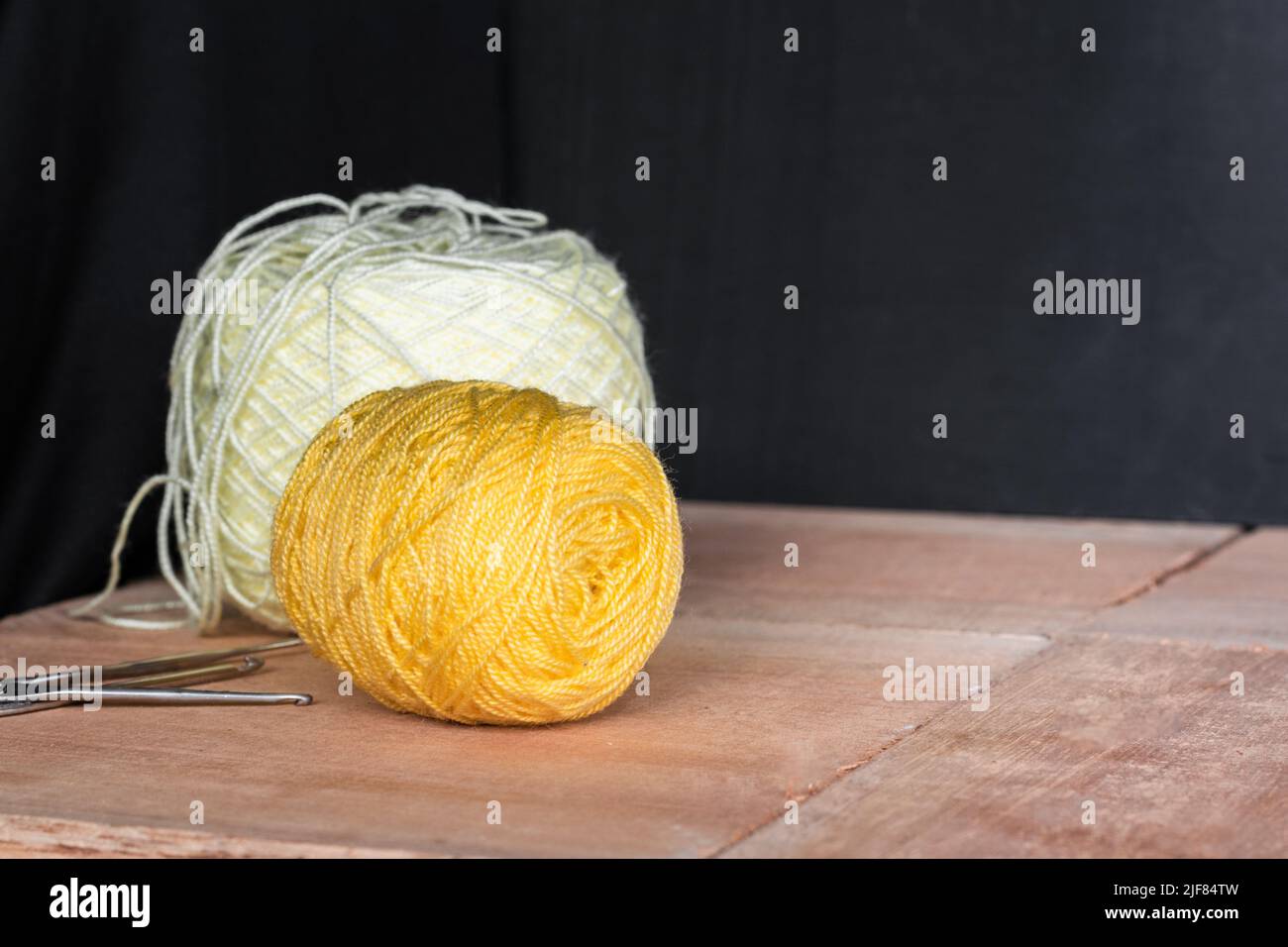 Zwei Rollen gelbes und weißes Garn zum Häkeln, auf schwarzem und orangefarbenem Holzhintergrund. Garn bereit zum Häkeln zu Hause. Work at Home Konzept. Stockfoto