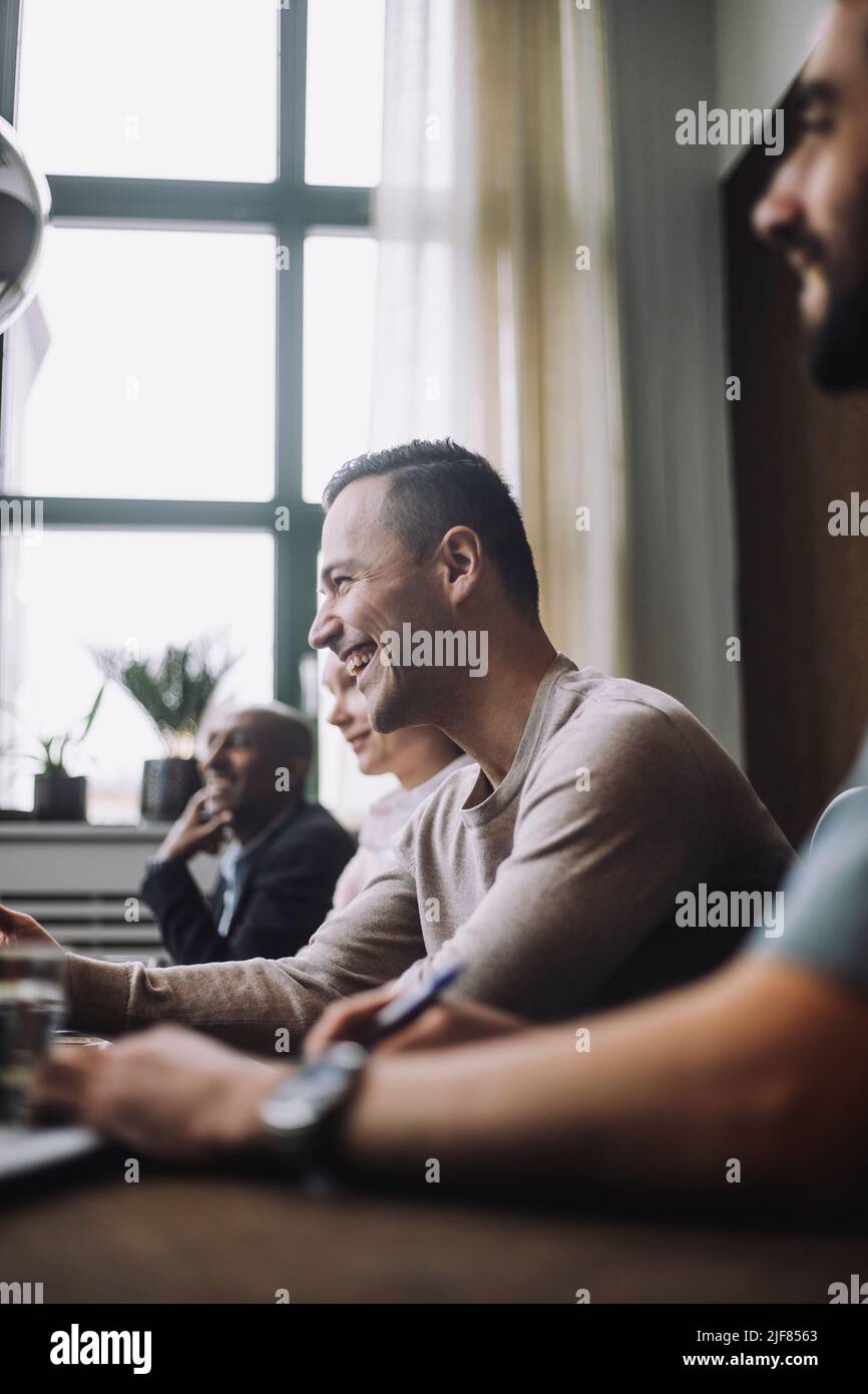Fröhlicher, reifer Geschäftsmann, der lachend bei Kollegen im Besprechungsraum sitzt Stockfoto